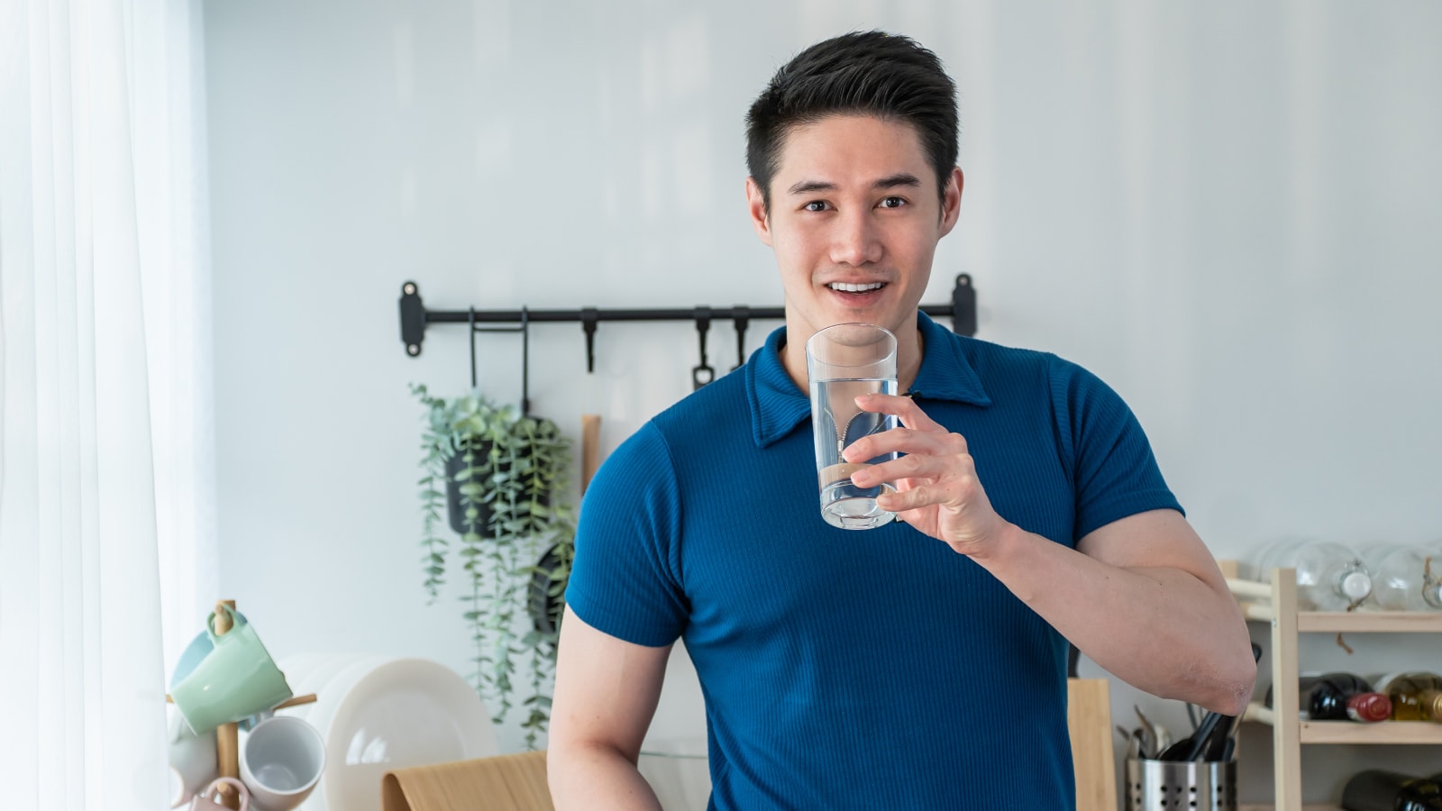 Pria muda minum air putih di dapur sebagai bagian dari gaya hidup sehat dan hidrasi alami